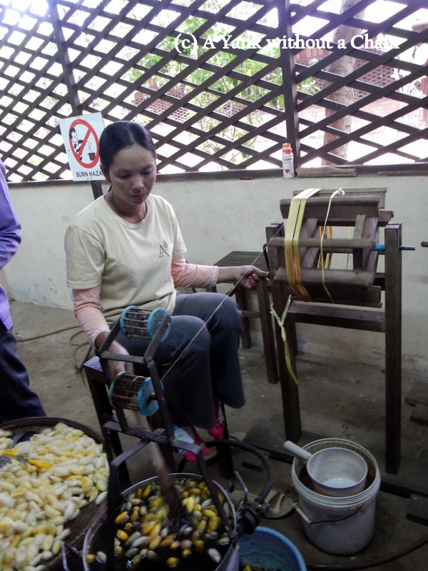 A woman turning silkworm cocoons into silk threads at the Artisans Angkor silk farm